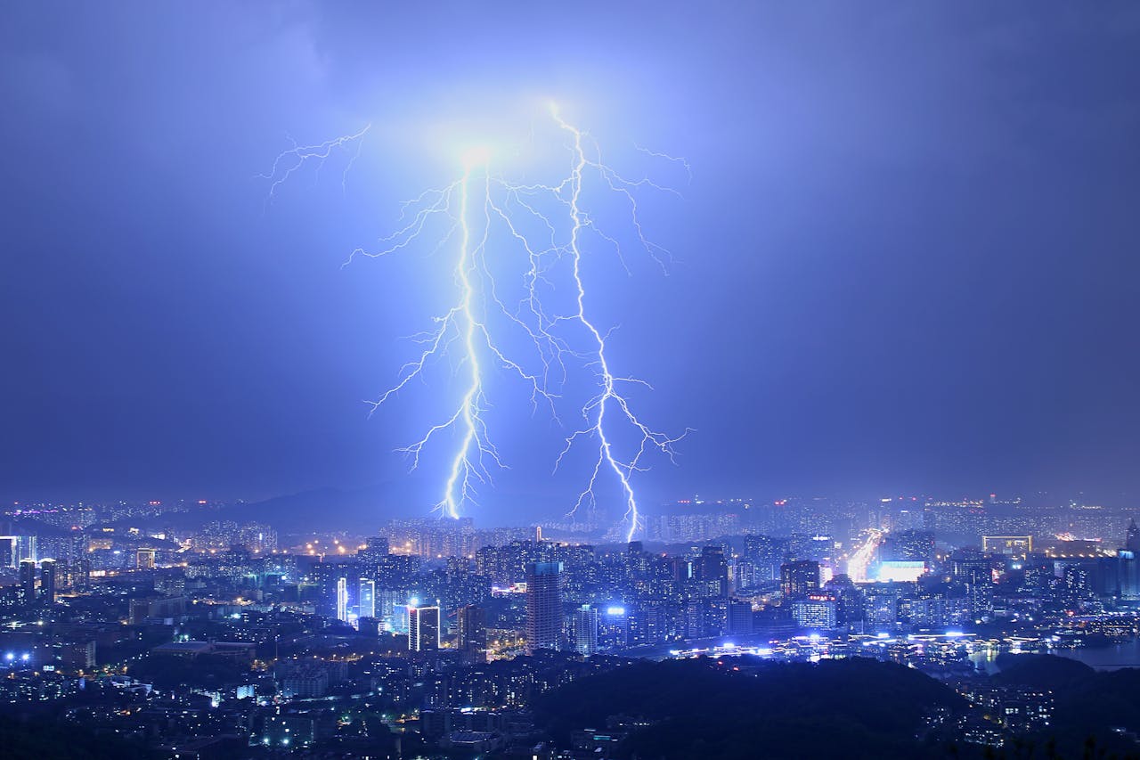 Breathtaking thunderstorm with lightning bolts over modern illuminated city at night with purple sky